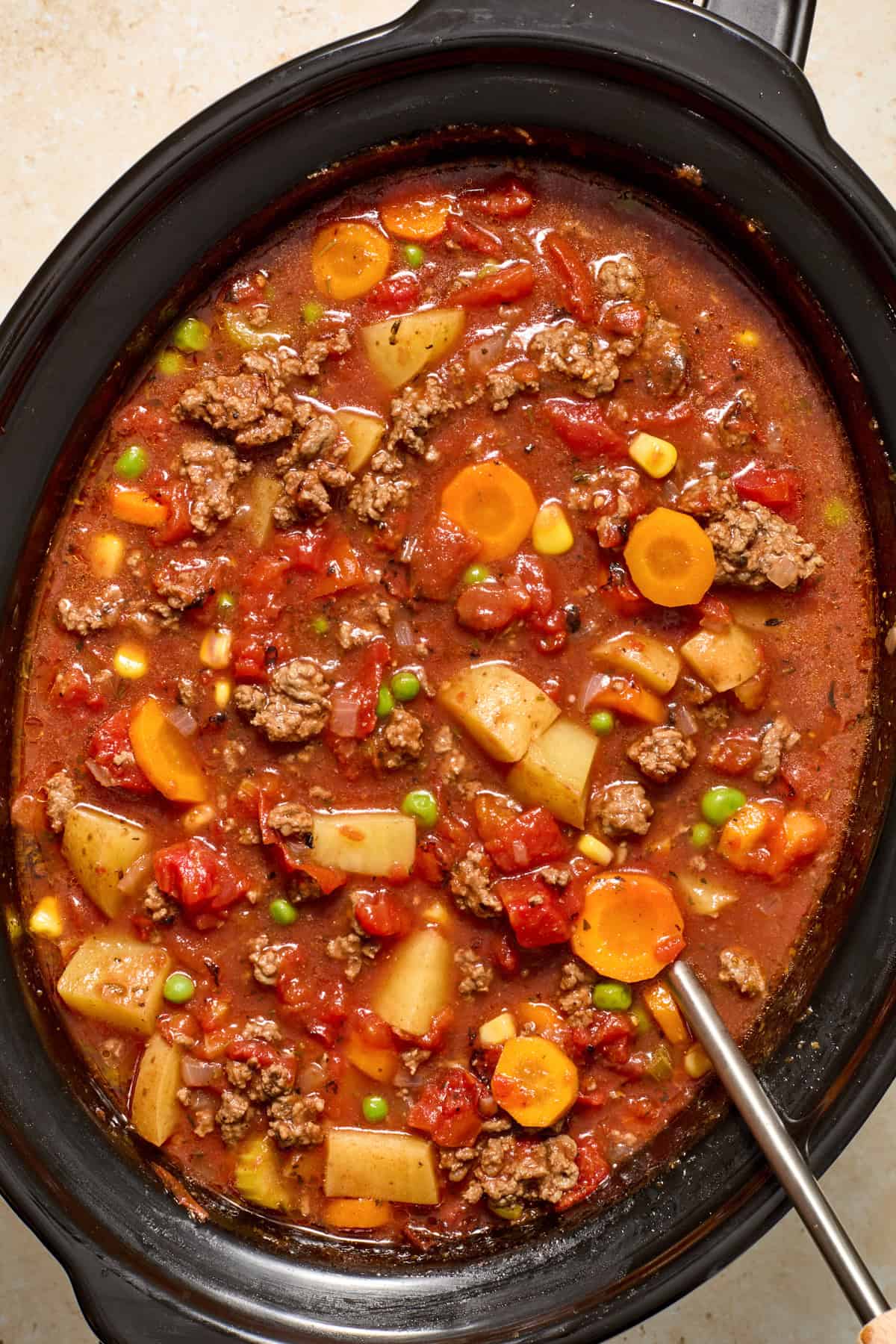 Prepared slow cooker hamburger vegetable soup in crockpot with ladle.