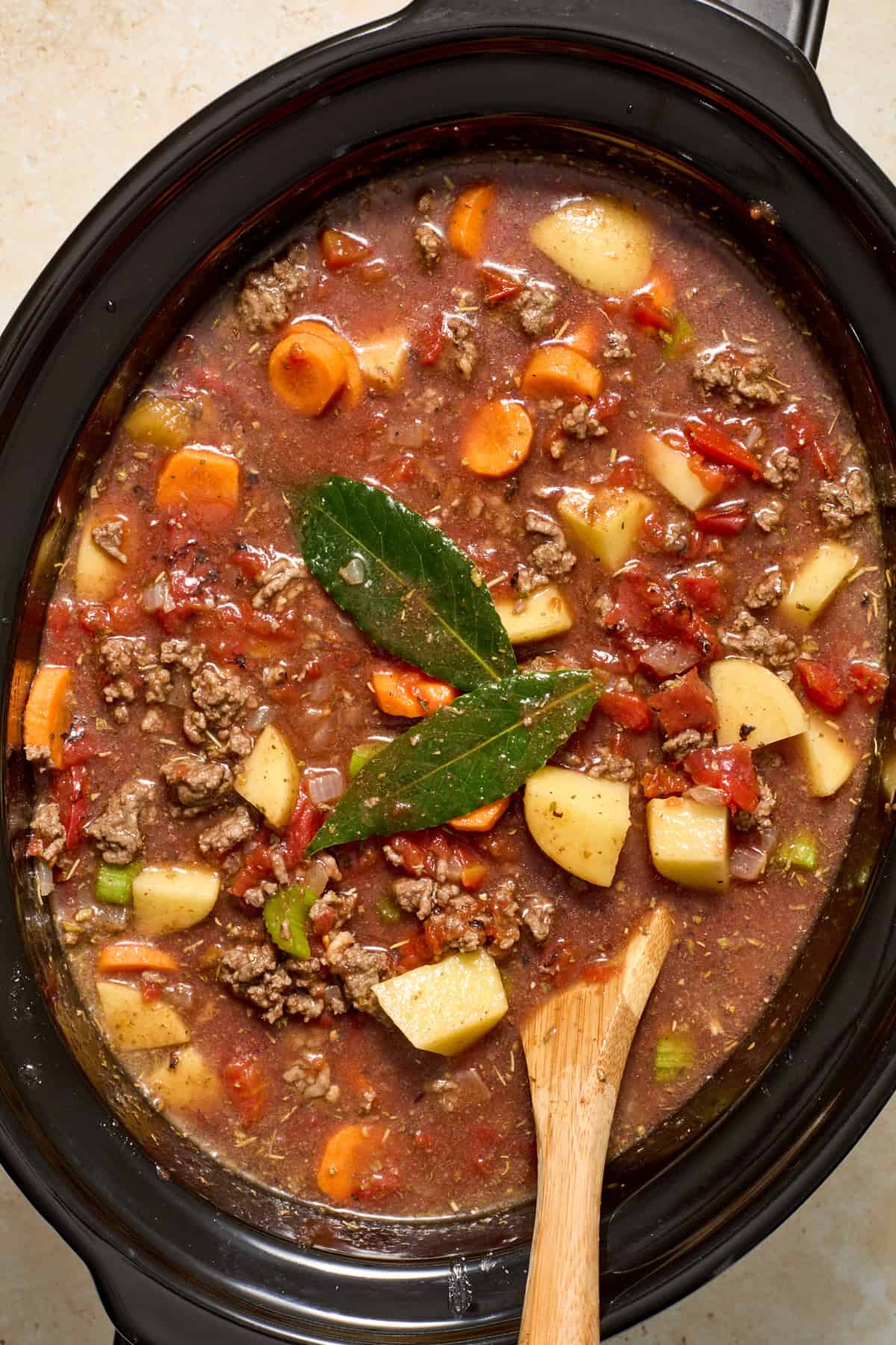 Broth and other ingredients added to crockpot with wood spoon.
