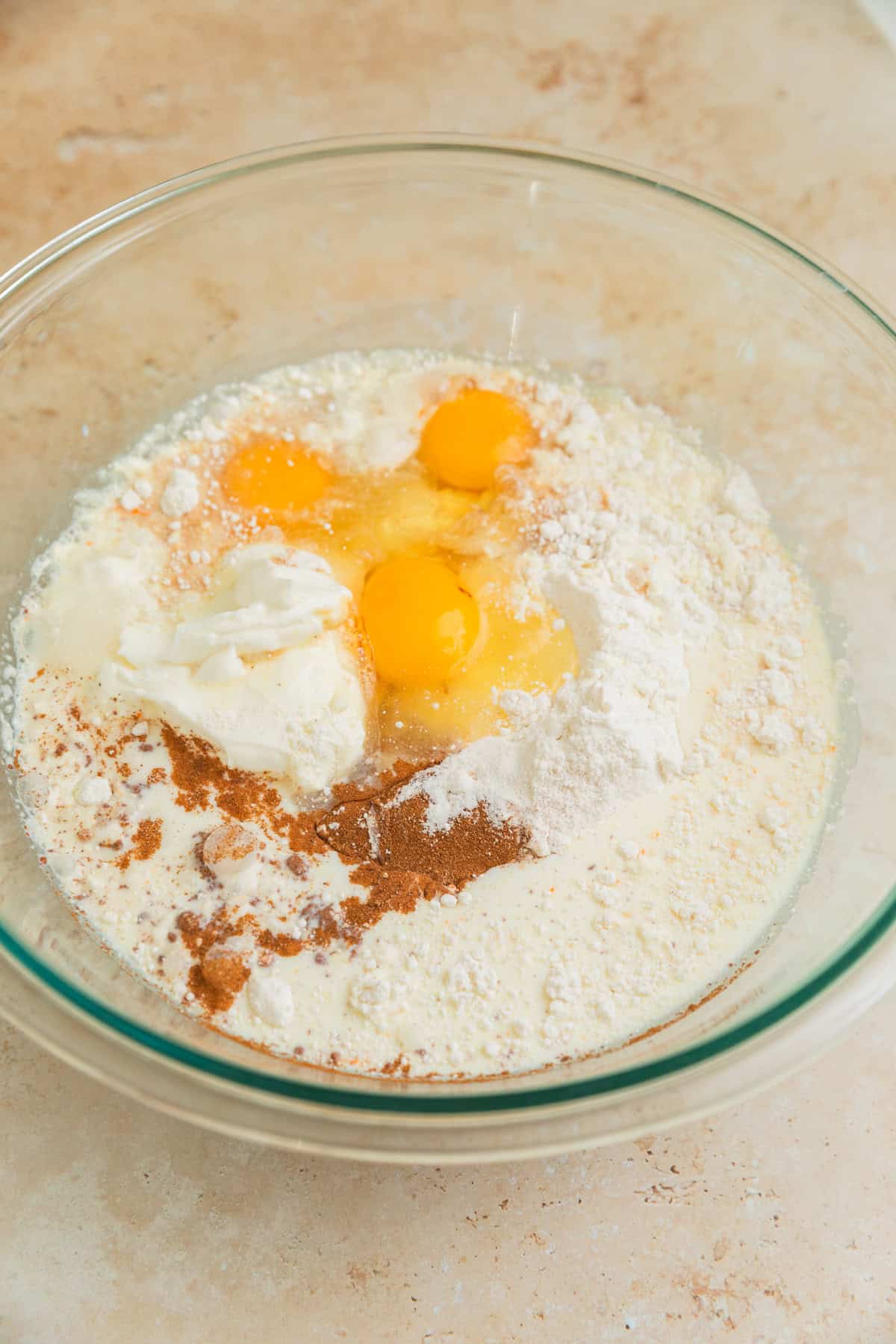 Cake mix, milk, eggs, oil and other ingredients in glass bowl before mixing.