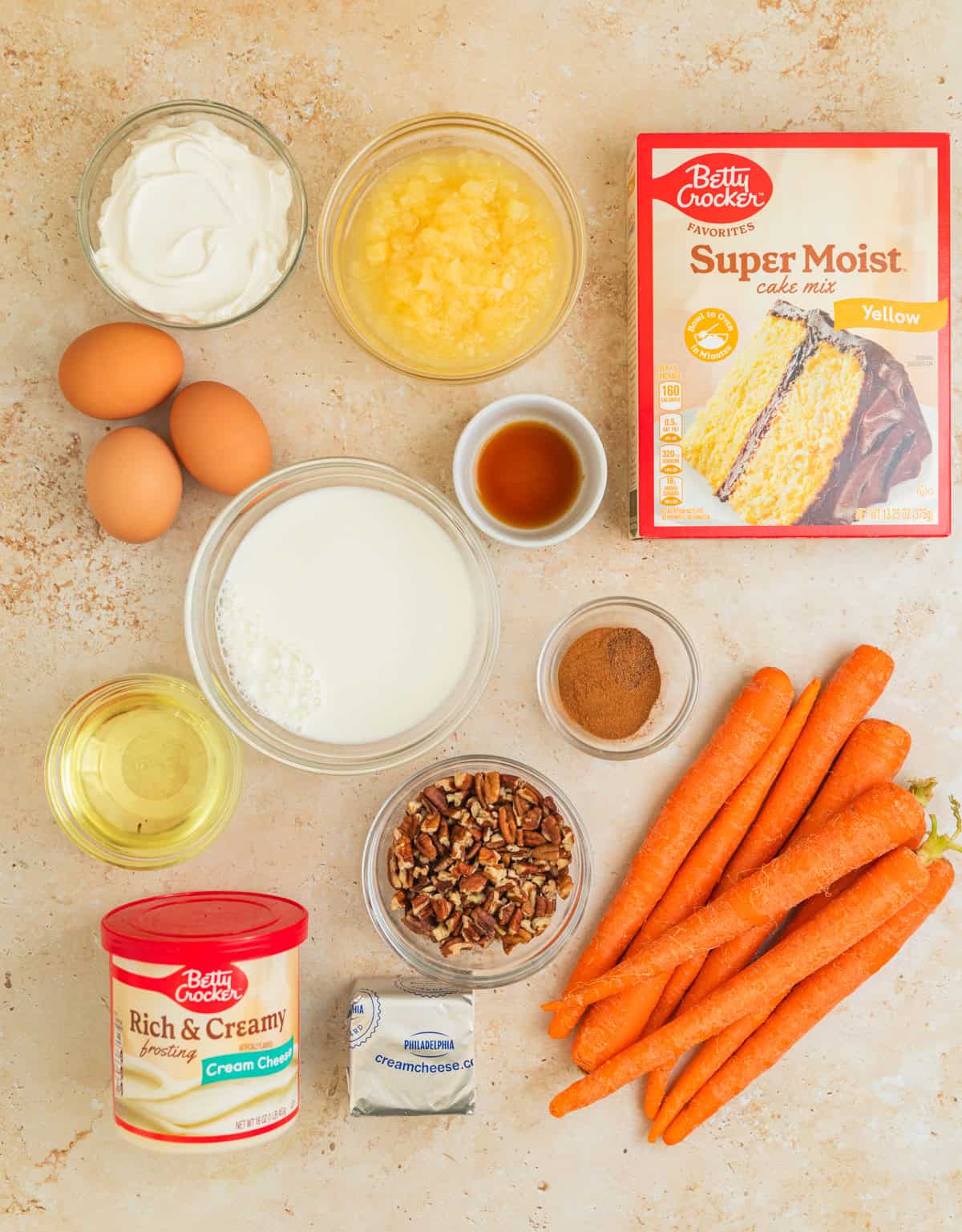 Yellow cake mix, carrots, pecans, milk, oil and other ingredients on surface.