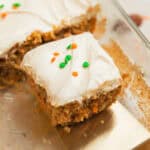 Slice of carrot cake with cream cheese frosting on spatula being pulled from the rest of the cake.