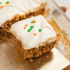 Slice of carrot cake with cream cheese frosting on spatula being pulled from the rest of the cake.