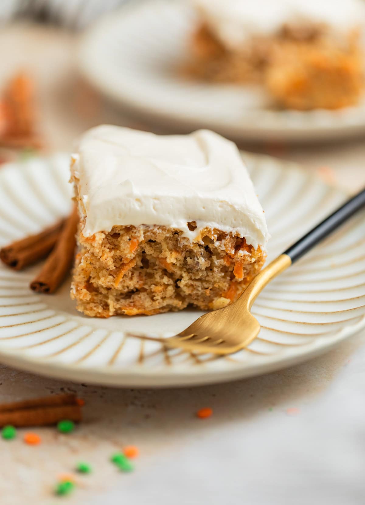 Slice of carrot cake made from cake mix on plate with fork and cinnamon sticks.