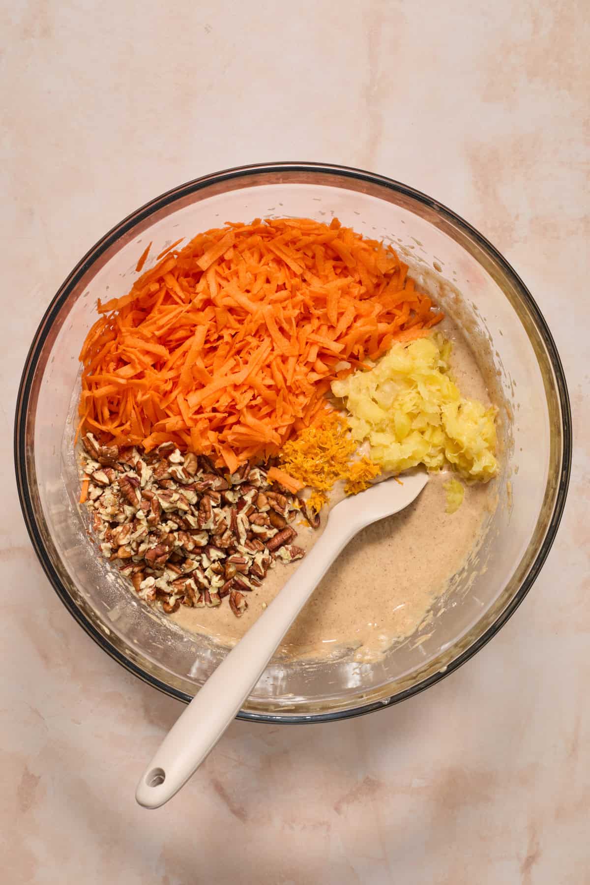 Shredded carrots, pecans and pineapple in bowl of cake batter before stirring.