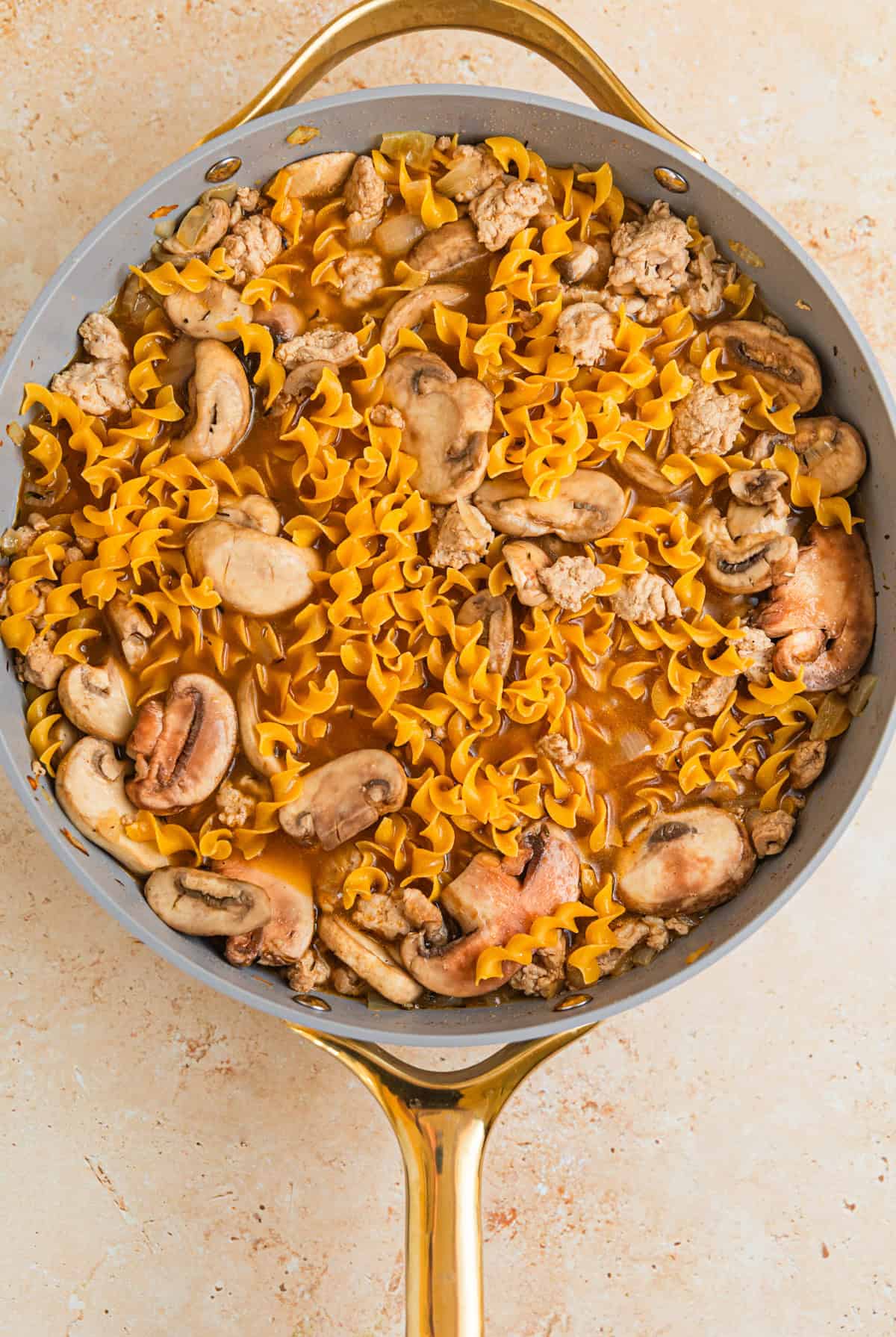 Broth and egg noodles added to skillet with meat and onions.