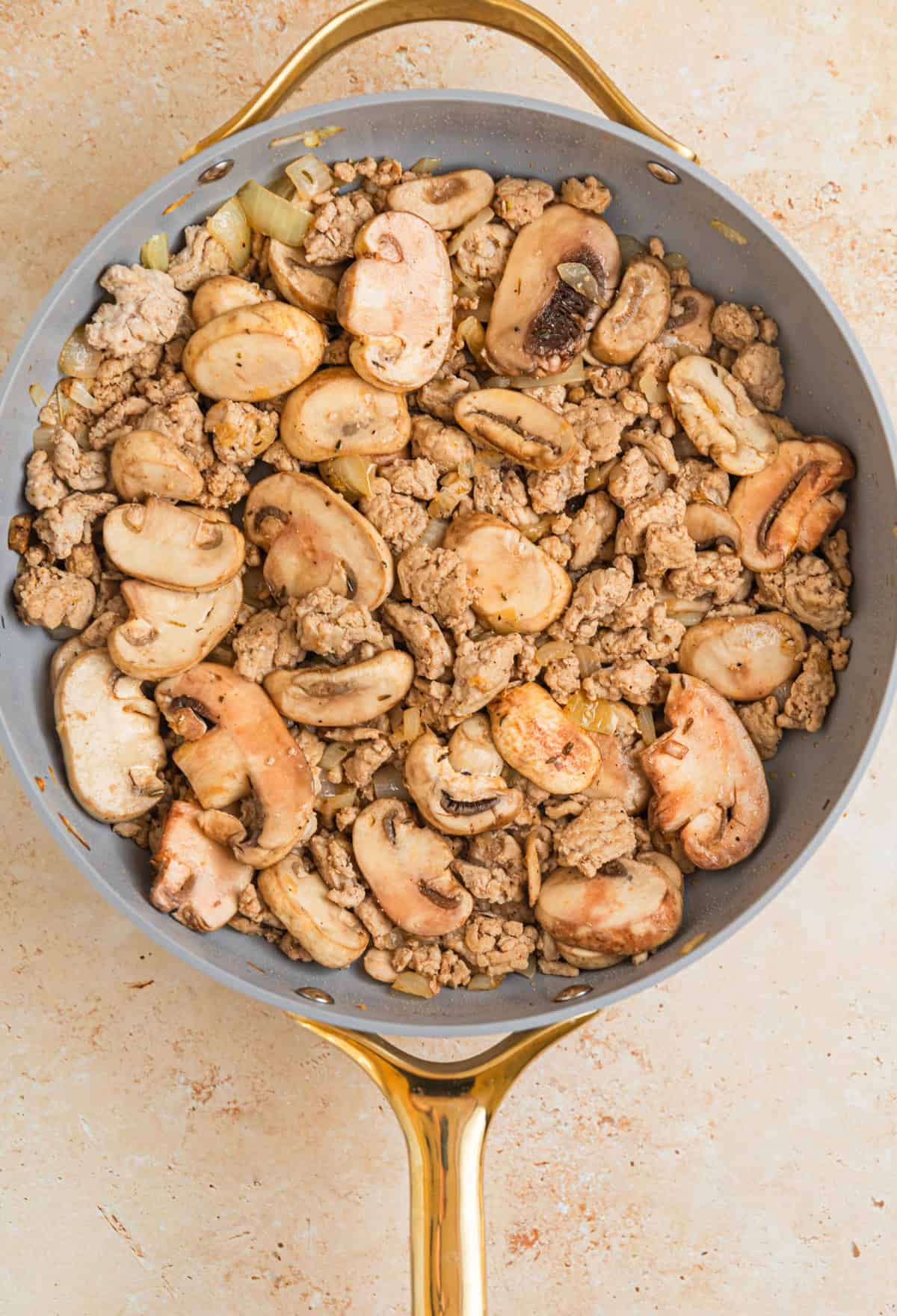 Mushrooms in skillet with browned ground turkey and onions.