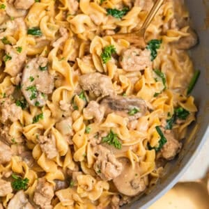 Skillet with ground turkey stroganoff with egg noodles and mushrooms and topped with chopped parsley.