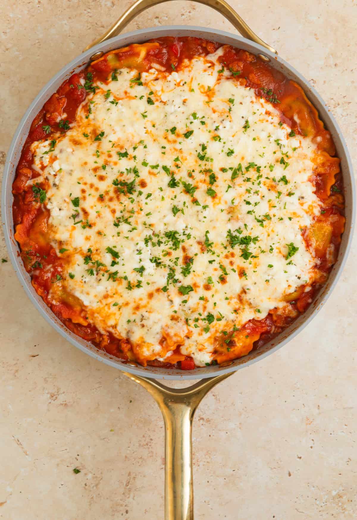 Skillet ravioli lasagna with cheese melted on top and parsley added.