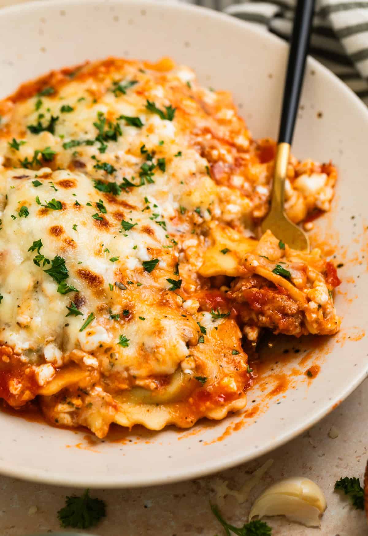 Plate with skillet lasagna ravioli with fork scooping in.