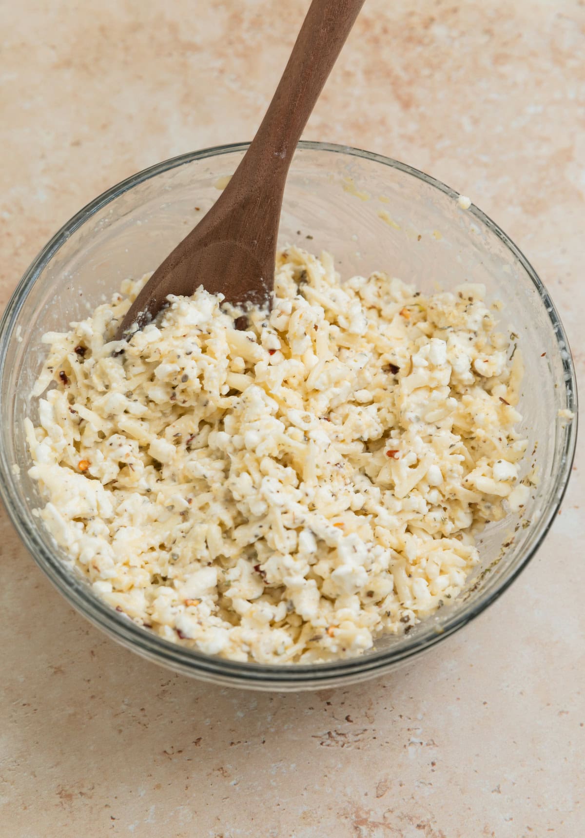 Cottage cheese lasagna mixture in bowl with wooden spoon.