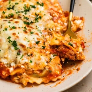 Skillet lasagna made with ravioli on plate with fork scooping up a forkful.