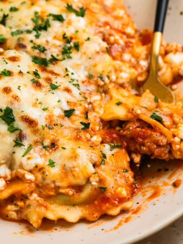 Skillet lasagna made with ravioli on plate with fork scooping up a forkful.