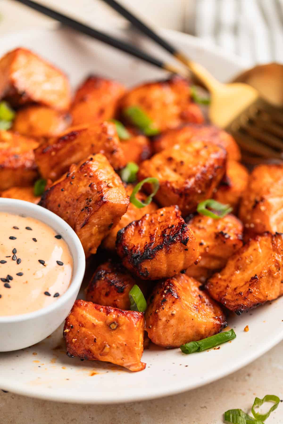 Air fried steak bites on plate topped with green onion and served with bang bang sauce in dish.