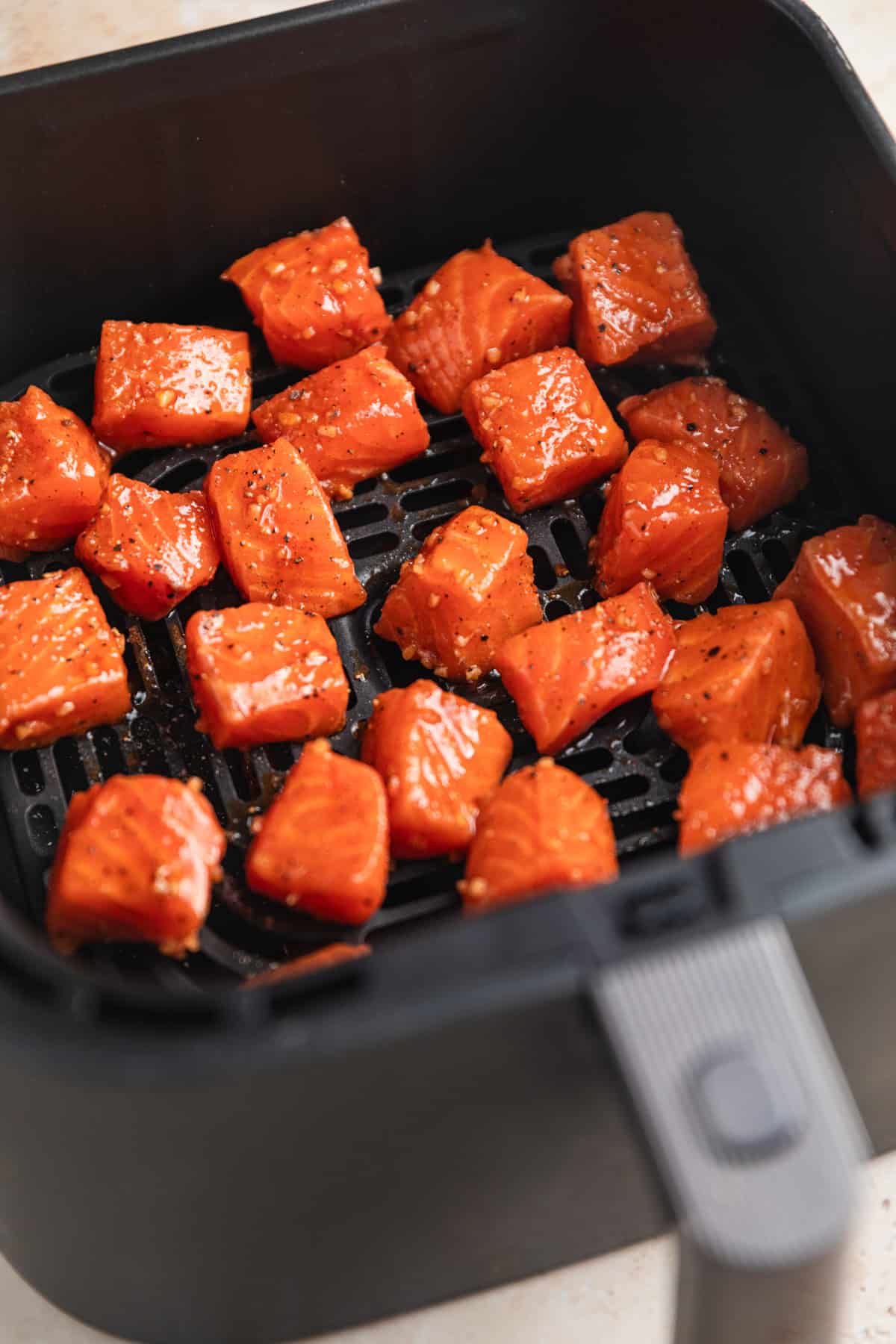 Raw salmon bites in air fryer basket before cooking.