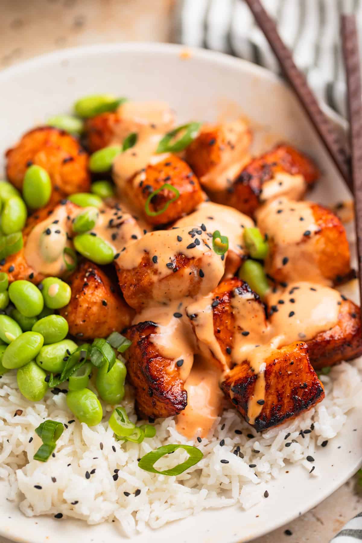 Dish with air fryer salmon bites topped with bang bang sauce and black sesame seeds.