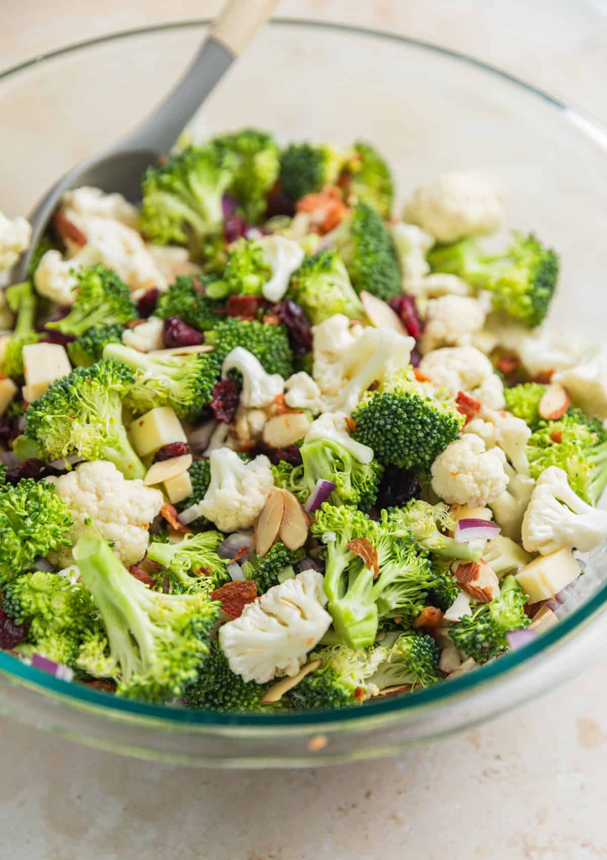 Tossed broccoli cauliflower salad in glass bowl with spoon before adding dressing.