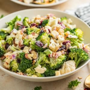 Broccoli cauliflower salad in bowl tossed with cheese, cranberries, bacon and more.
