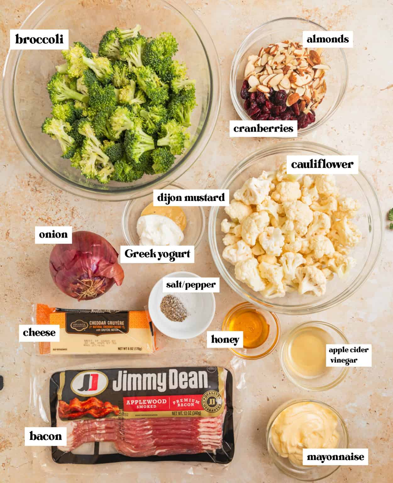 Bacon, mayo, almonds, broccoli florets, cauliflower and other ingredients for recipe arranged on surface with labels.