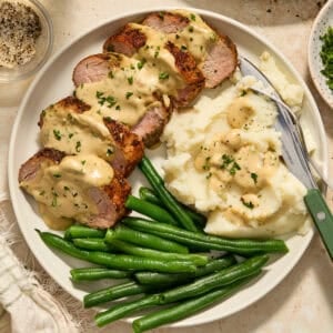 Plate with pork tenderloin topped with mustard sauce and parsley.