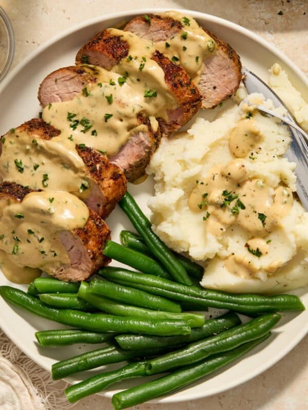 Plate with pork tenderloin topped with mustard sauce and parsley.