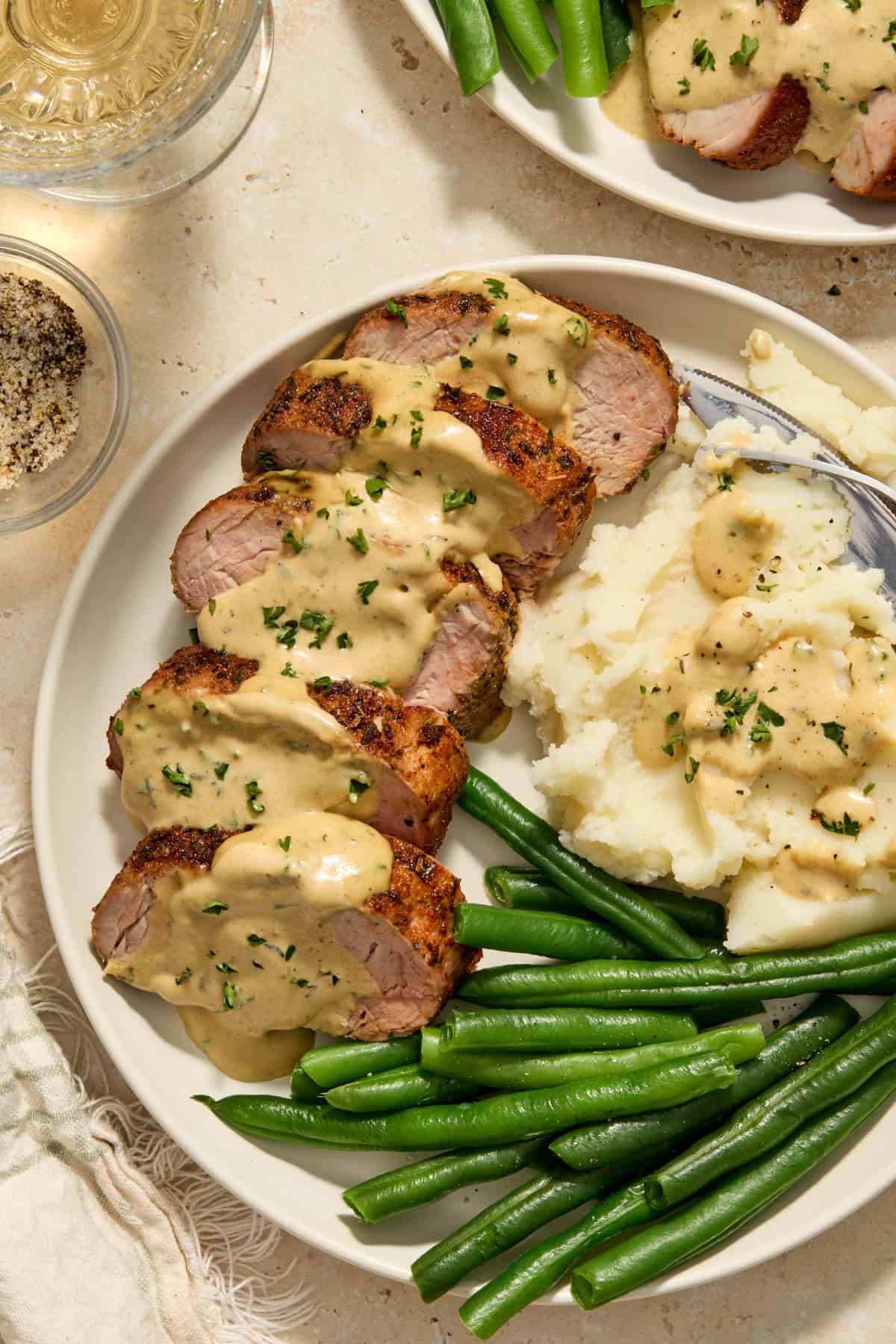 Plate with sliced pork tenderloin topped with creamy mustard sauce served with mashed potatoes and green beans.