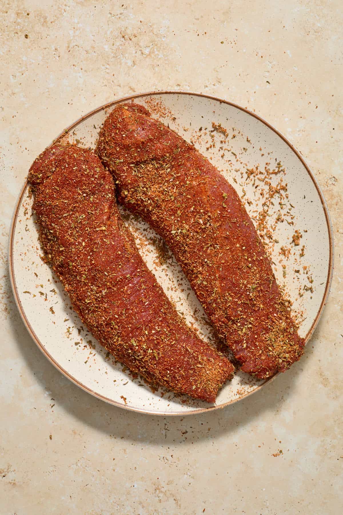 Pork tenderloin on plate with spice rub covering it.