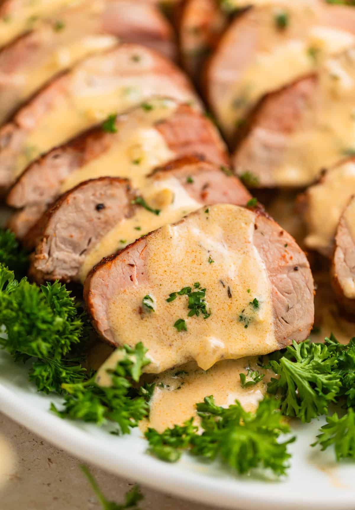 Roasted pork tenderloin sliced on plate with creamy mustard sauce poured over top.