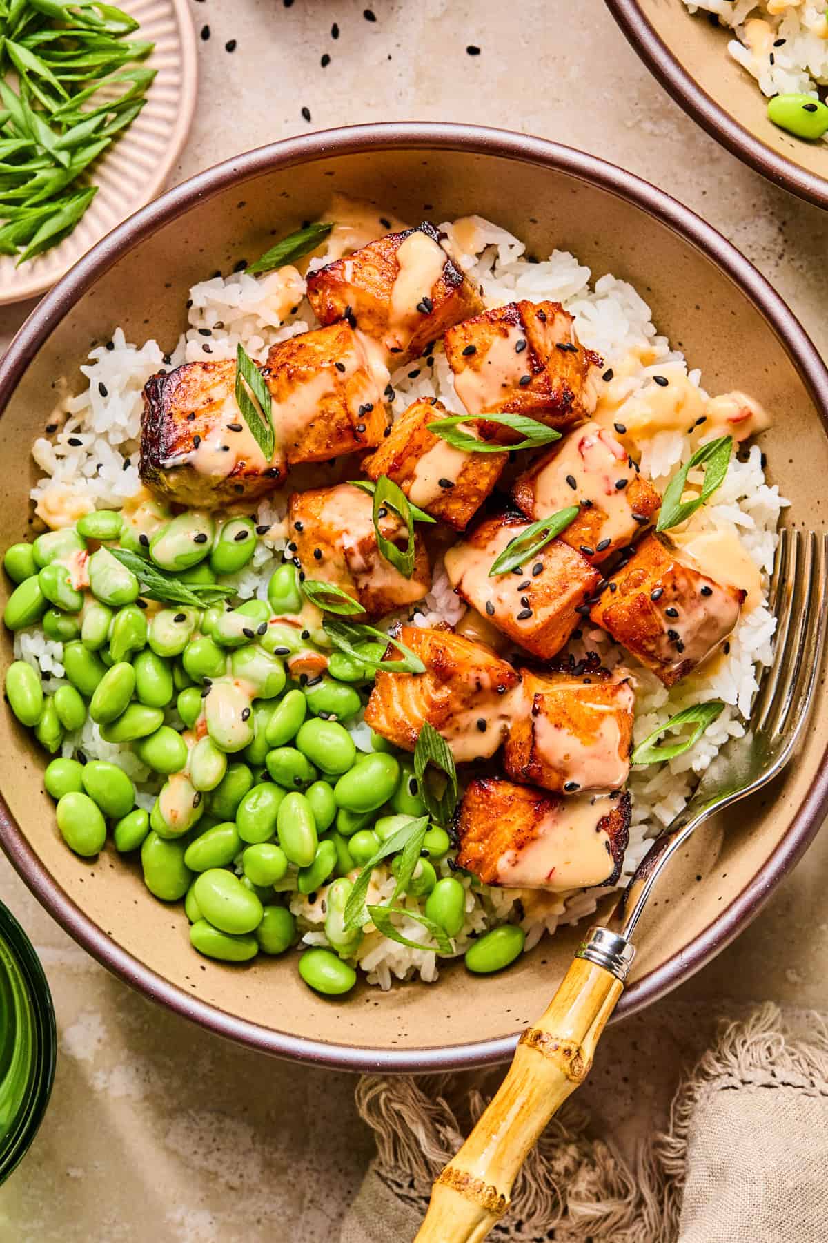 Dish with air fryer salmon bites topped with bang bang sauce and black sesame seeds.