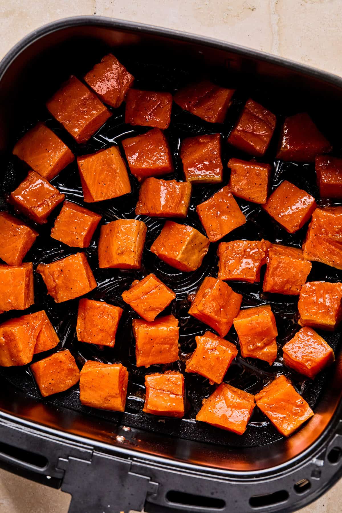 Raw salmon bites in air fryer basket before cooking.