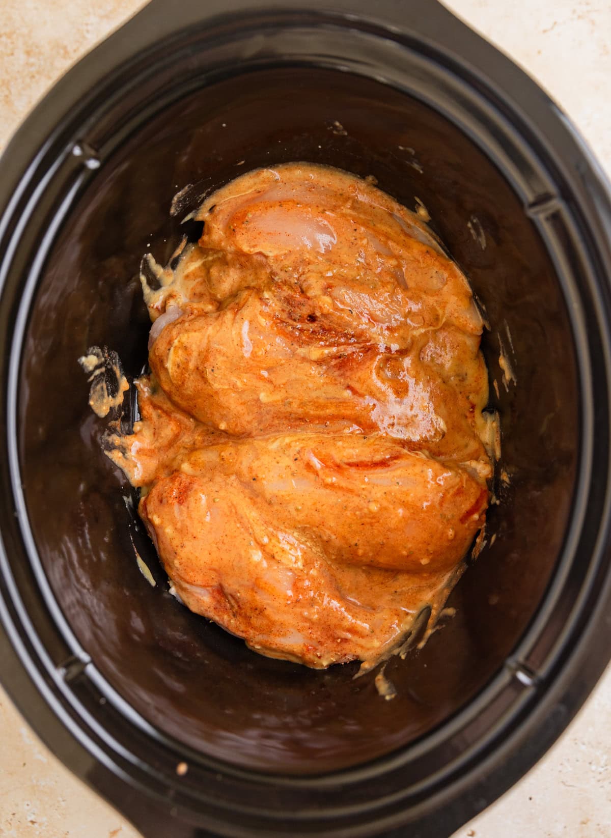 Raw chicken breasts in slow cooker topped with honey mustard sauce.