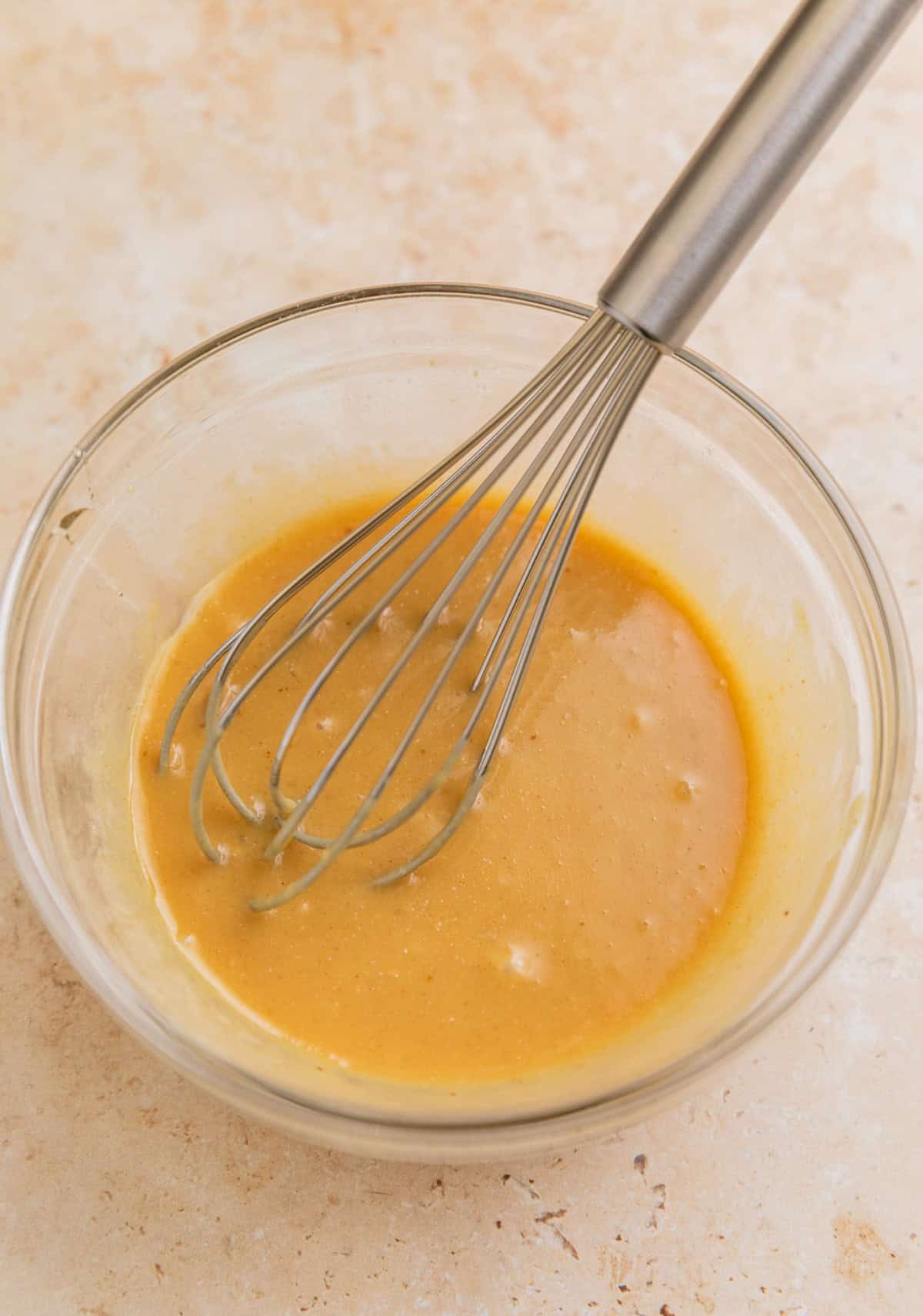 Honey mustard sauce in glass bowl with whisk.