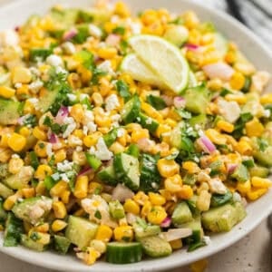 Cucumber corn salad in serving dish topped with chopped jalapeño and cilantro.