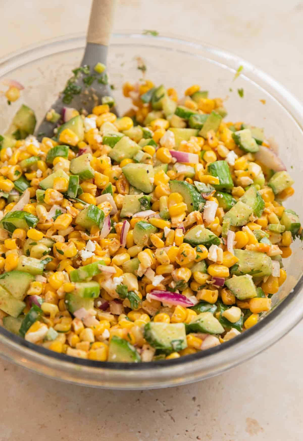 Prepped cucumber corn salad in glass bowl with spoon.