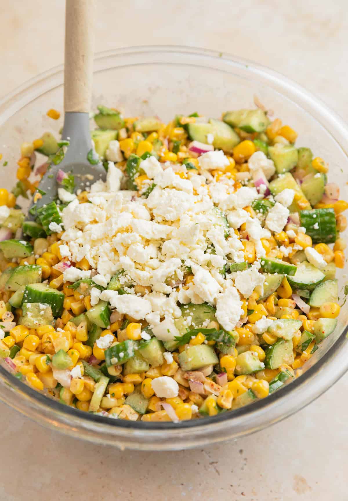 Tossed cucumber corn salad in bowl with feta cheese added on top before mixing.