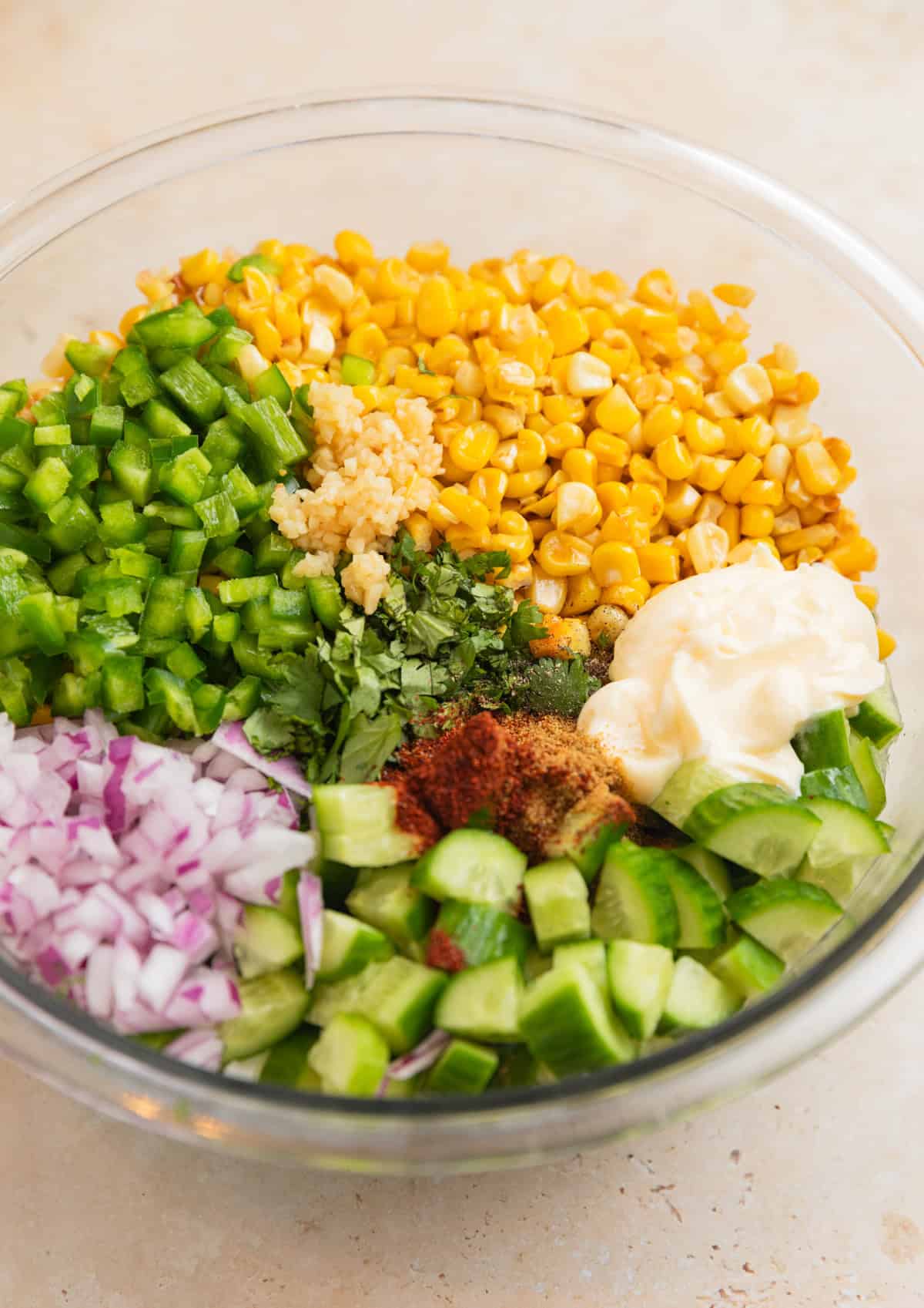 Corn, chopped cucumber, onion, mayo, and other ingredients in bowl.