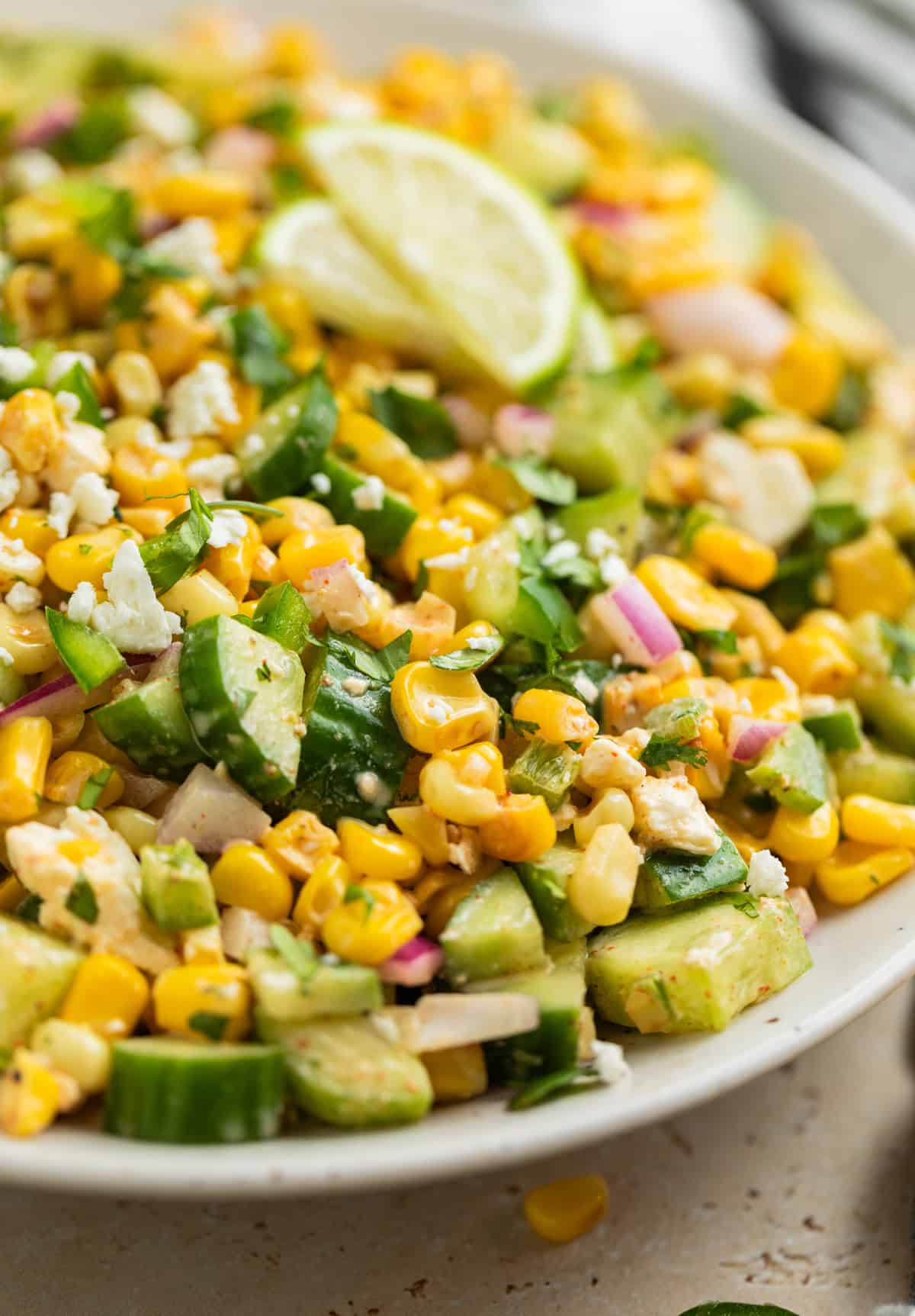 Corn and cucumber salad in white dish with lime slices.
