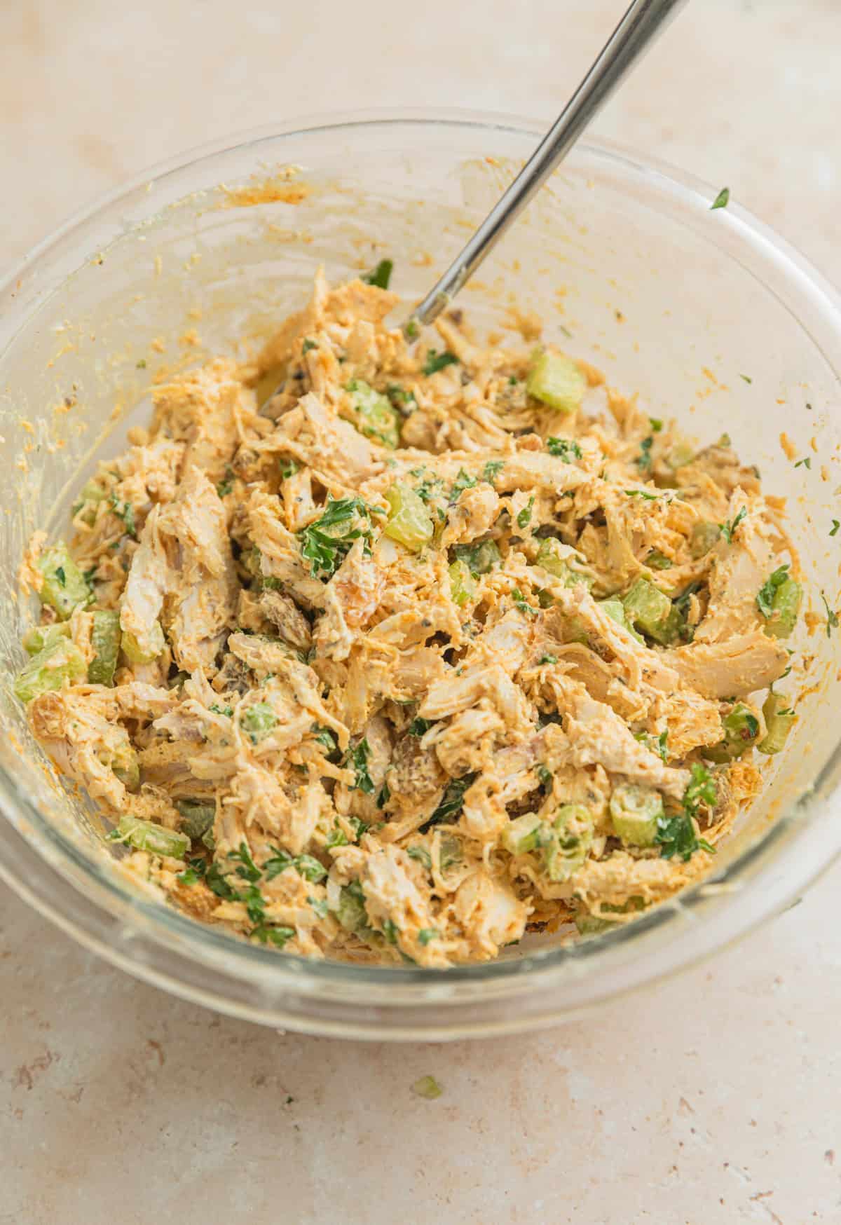 Mixed curry chicken salad in glass mixing bowl with spoon.