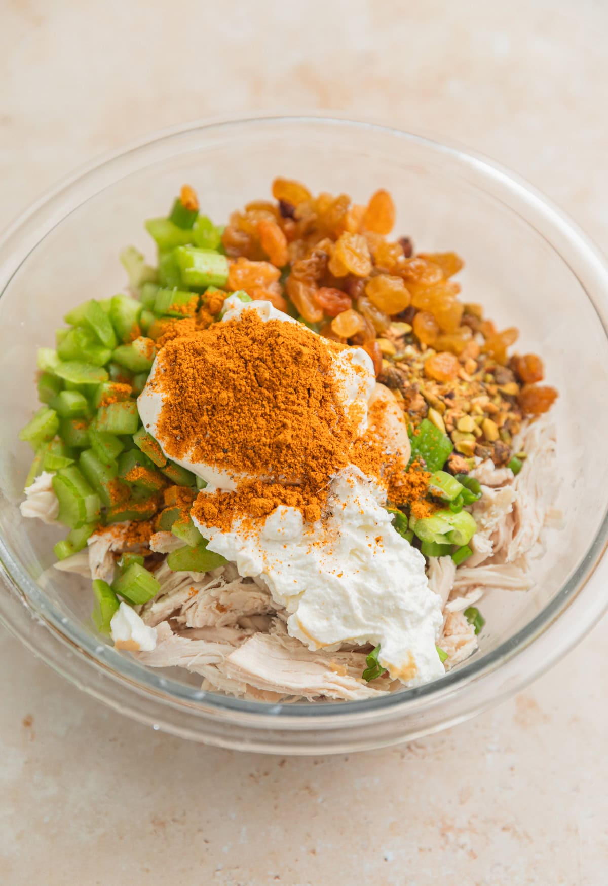 Shredded chicken, celery, golden raisins, curry powder and other chicken salad ingredients in glass bowl.