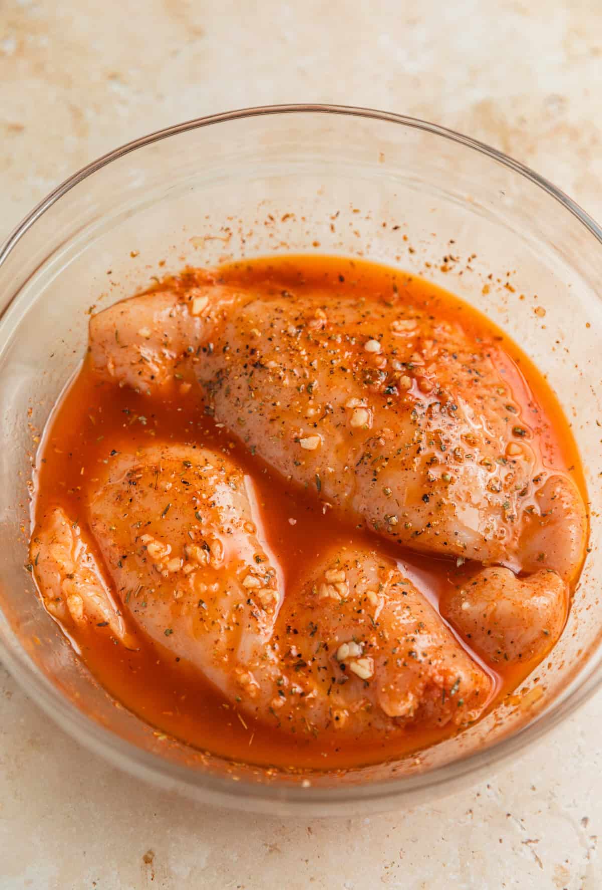 Chicken breast in marinade in glass bowl.