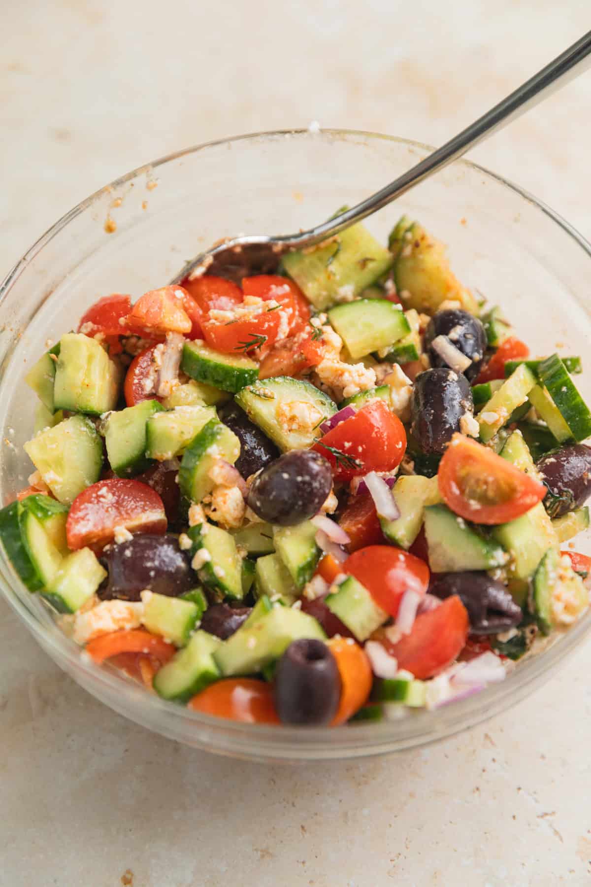 Cucumber feta salad in glass bowl with spoon.