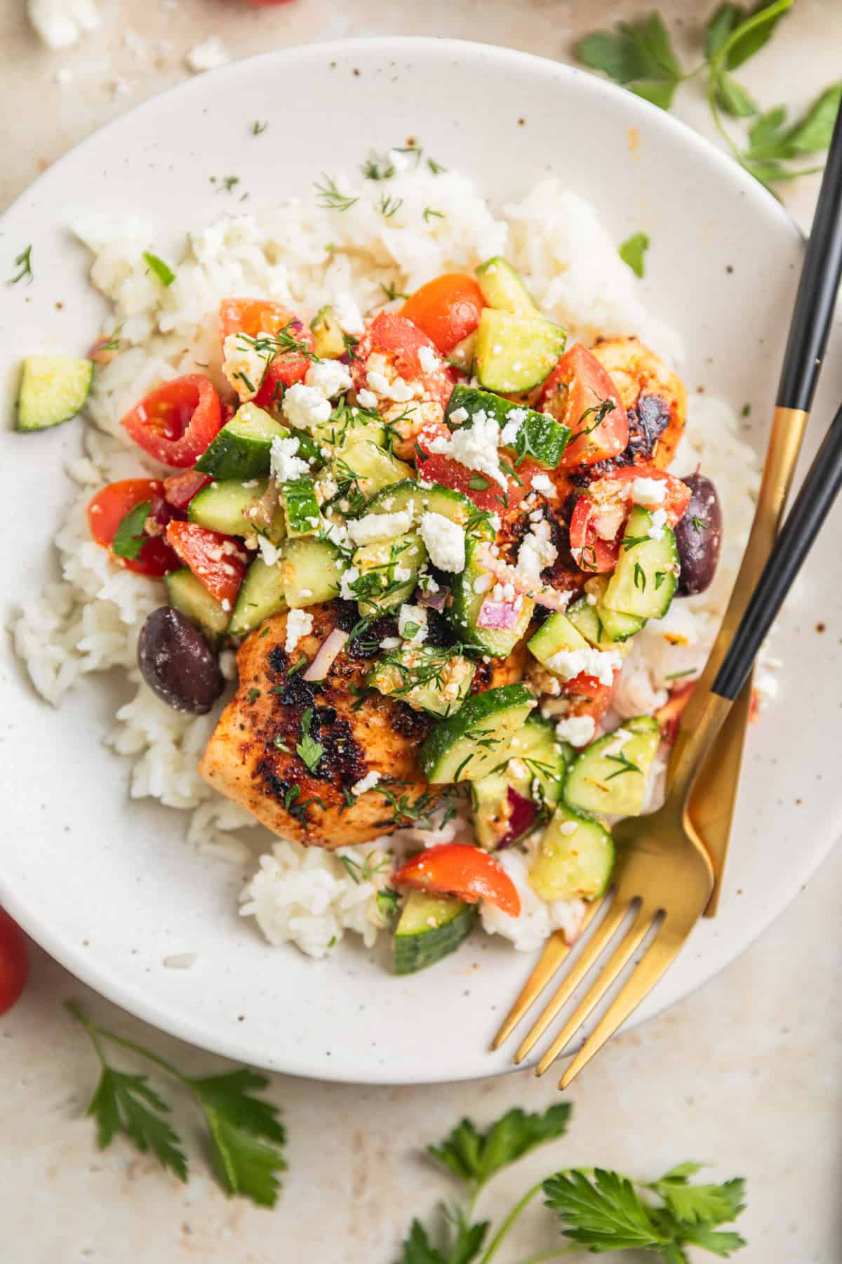 Grilled chicken on plate over rice topped with cucumbers, feta, olives and dill.