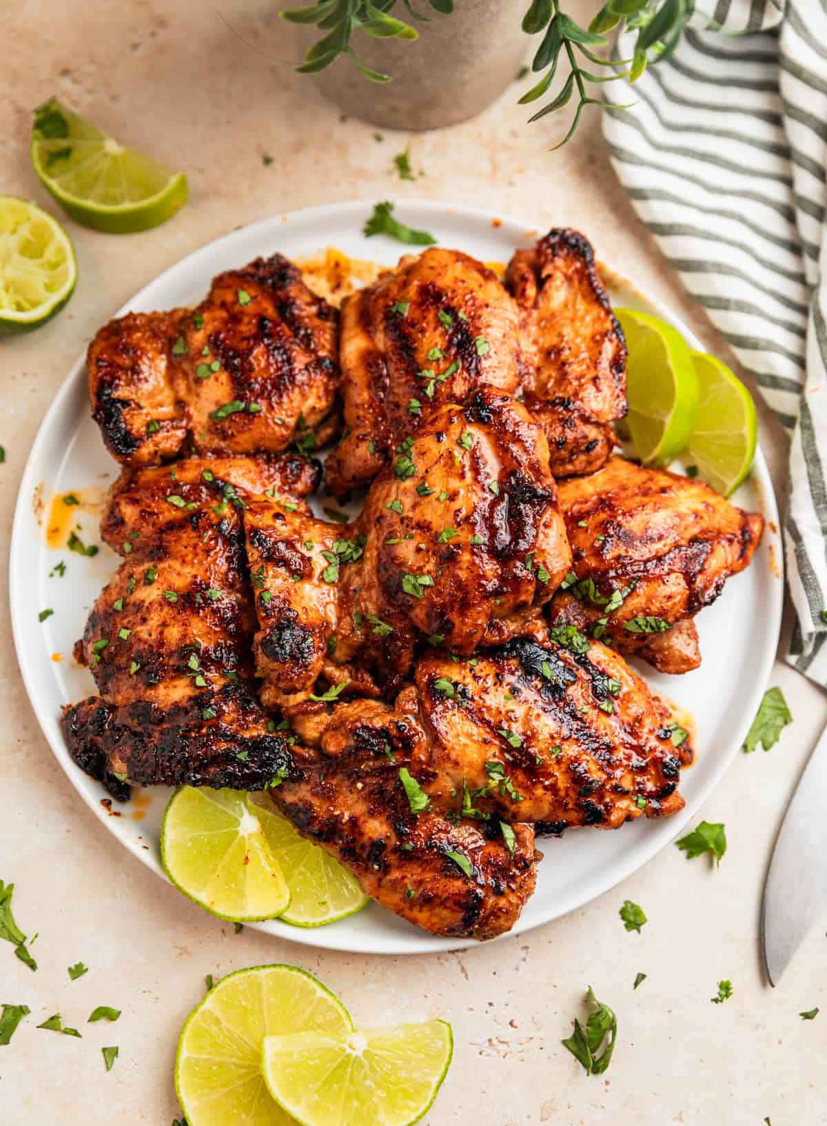 Grilled chicken thighs on white plate with sliced limes.