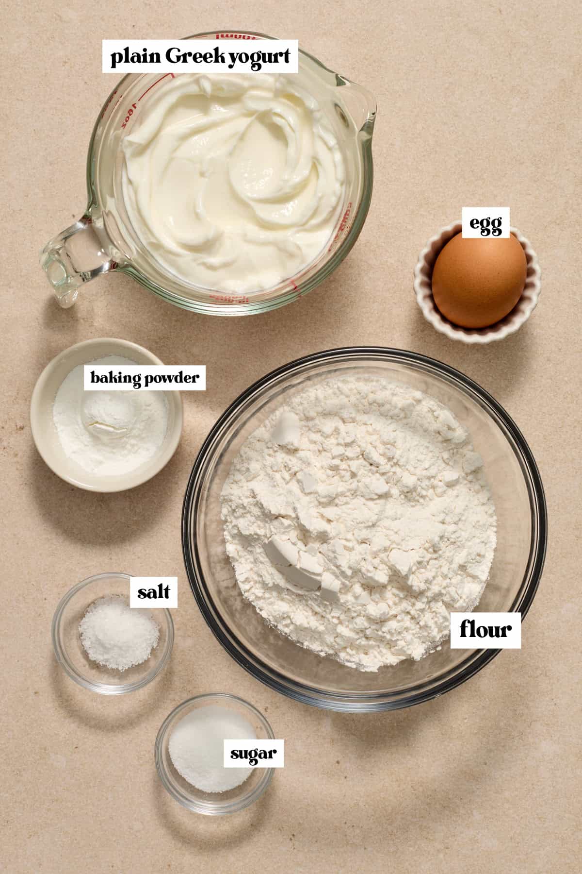 Flour, plain greek yogurt, egg and other ingredients to make recipe on surface.