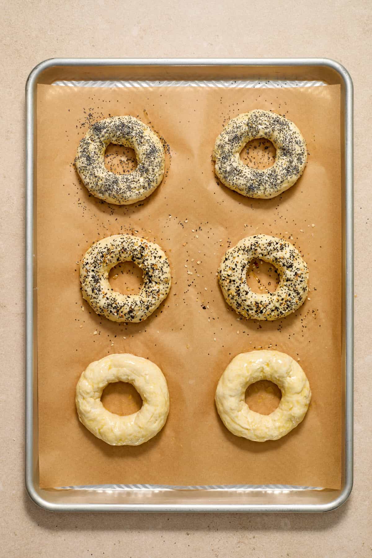 Egg washed bagels with poppy seeds and other ingredients on top.
