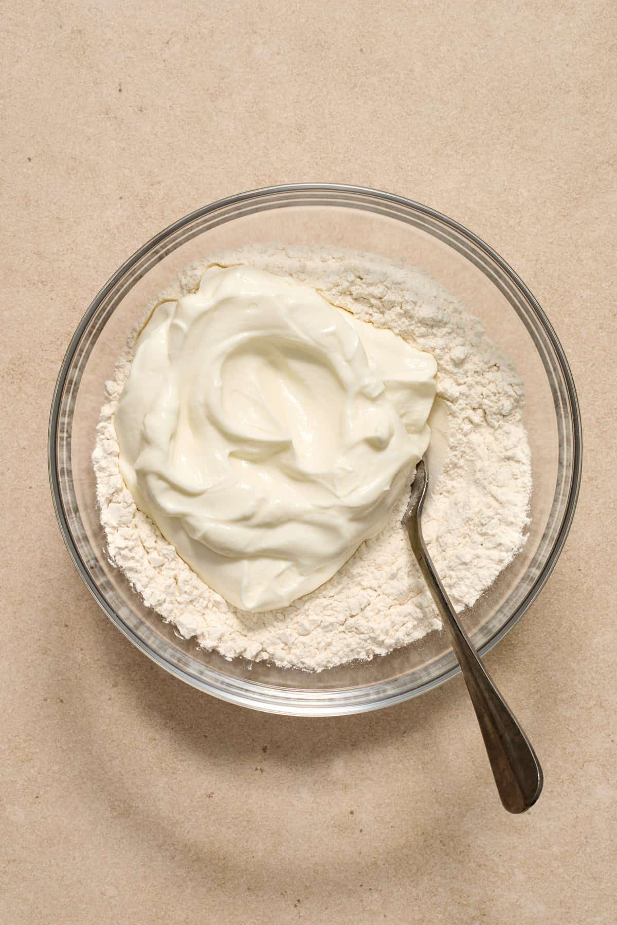 Greek yogurt added to bowl with flour and spoon.