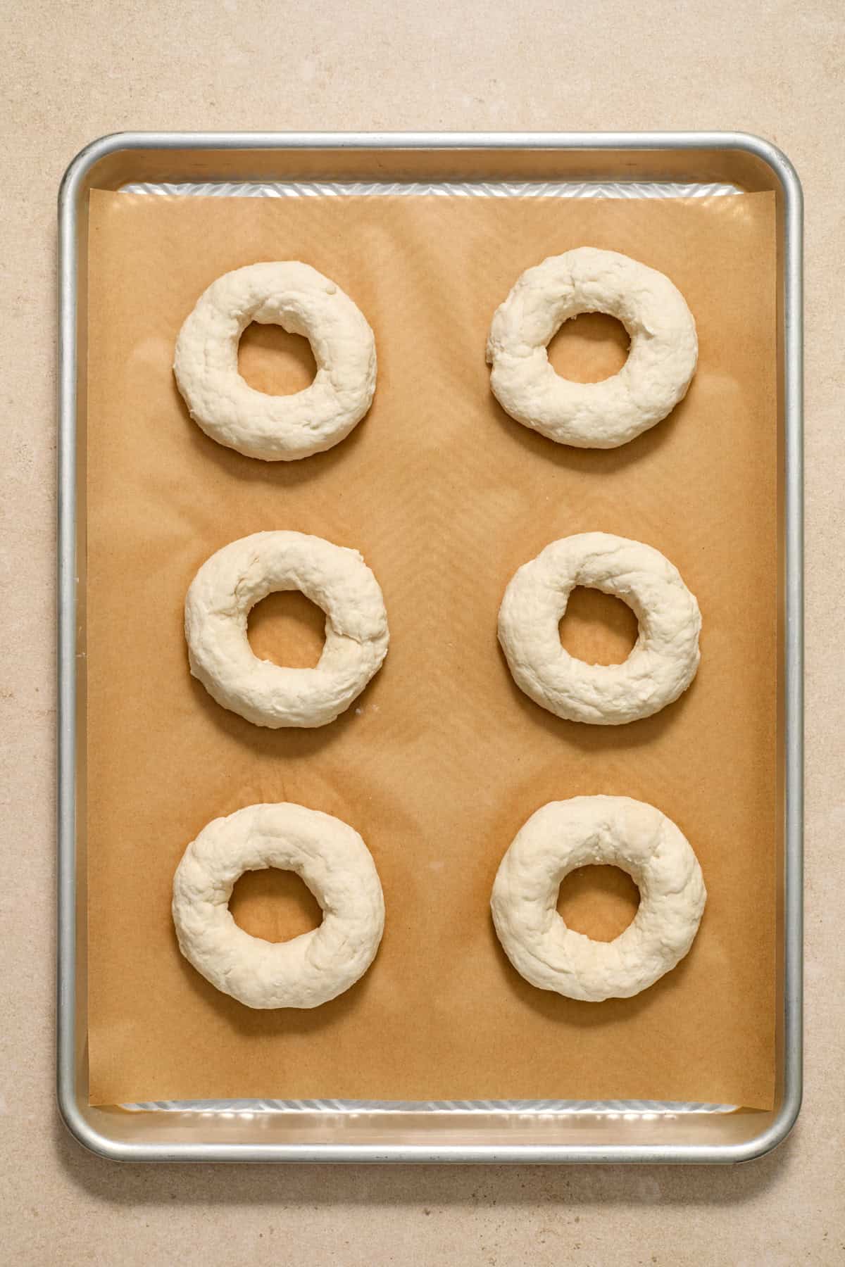 Bagels formed and arranged on parchment paper lined cookie sheet.