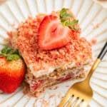 Layered strawberry icebox cake topped with strawberry crunch on plate with fresh strawberry garnish.