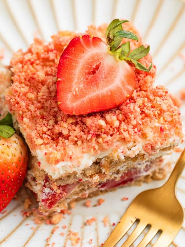 Layered strawberry icebox cake topped with strawberry crunch on plate with fresh strawberry garnish.