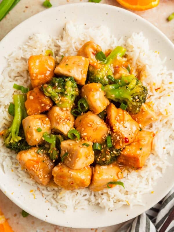Orange chicken and broccoli served over white rice on plate.
