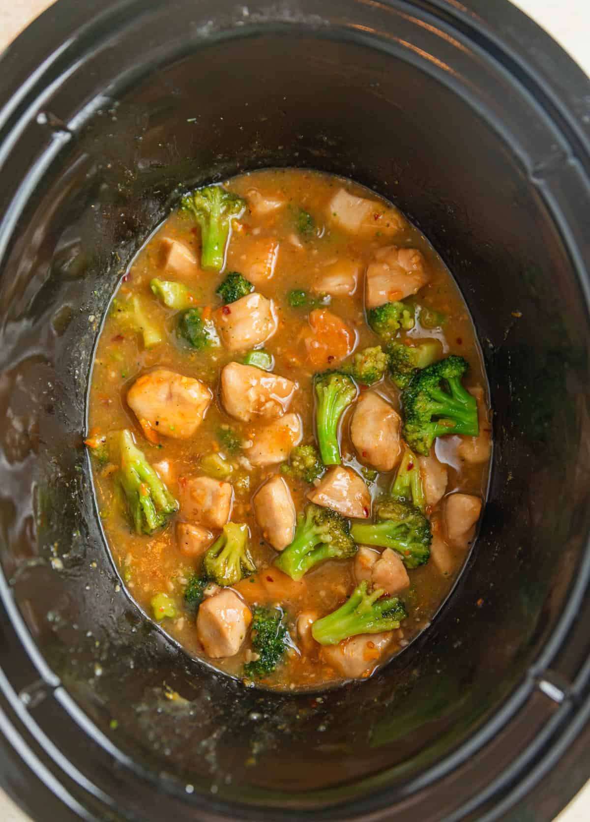 Slow cooker pot with orange broccoli and chicken cooked in sauce.